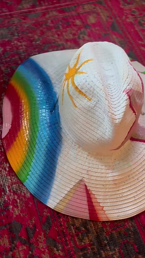 Full view of a white beach hat with hand-painted rainbow and sun/star designs