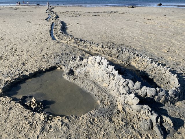 Long sand fortification with a water-filled moat leading toward the ocean