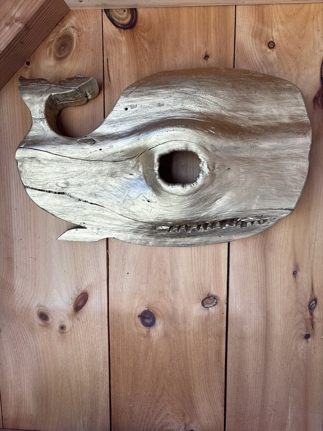 Carved wooden whale sculpture mounted on a wood-plank wall